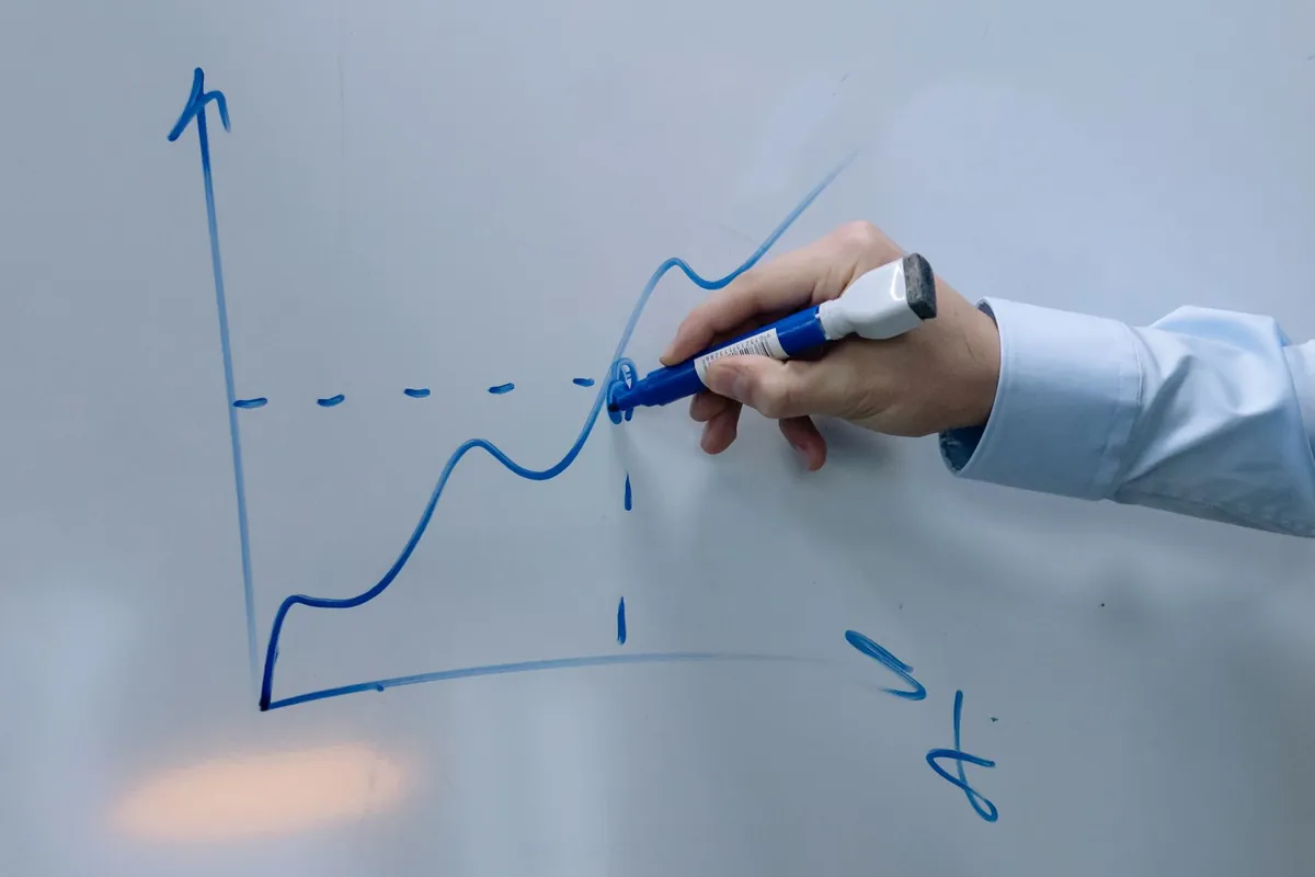 A hand drawing a graph on a whiteboard with a blue marker.