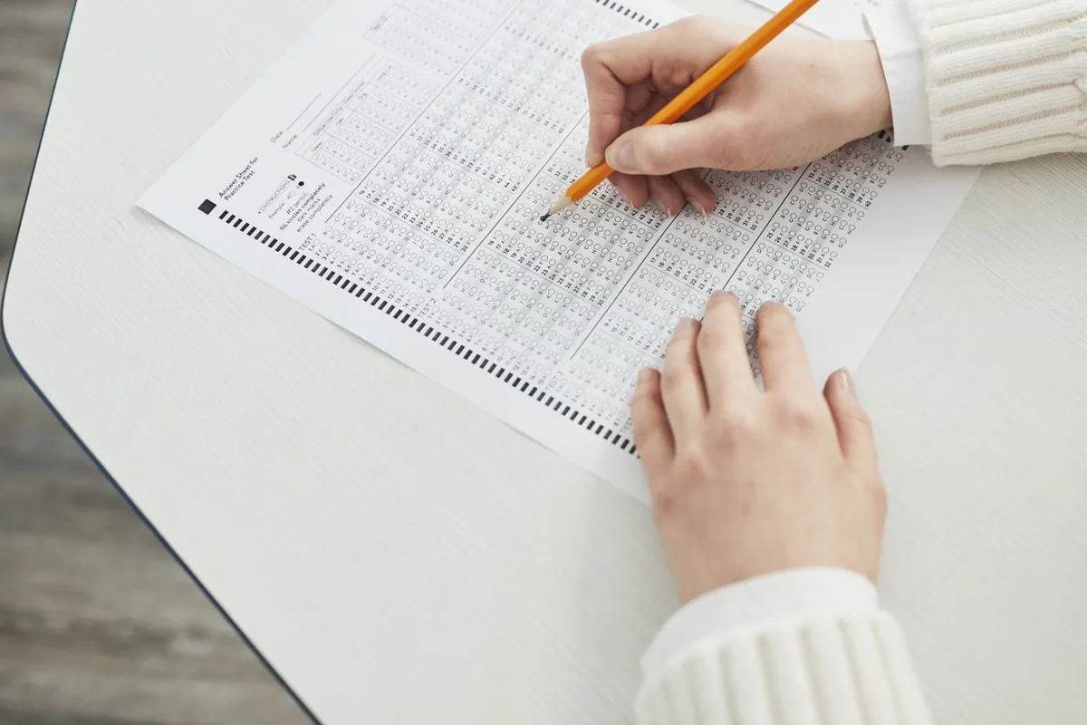 A pupil's hands filling in a multiple-choice answer sheet with a pencil.